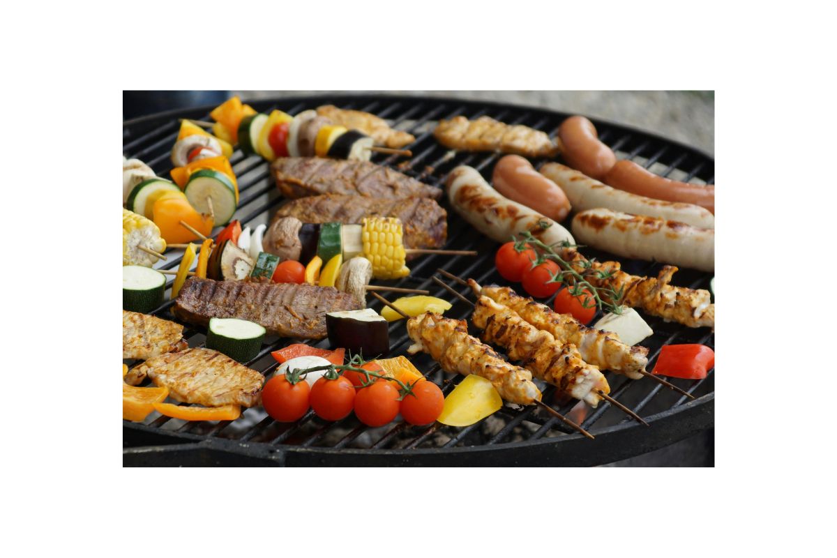 Grilled meats and vegetables on a barbecue grill, including skewers of chicken, sausages, and an assortment of colorful vegetables.